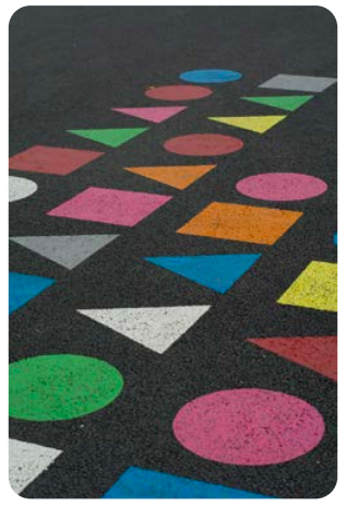 pattern of circles, squares, and triangles in bright colors contrasted on an asphalt surface