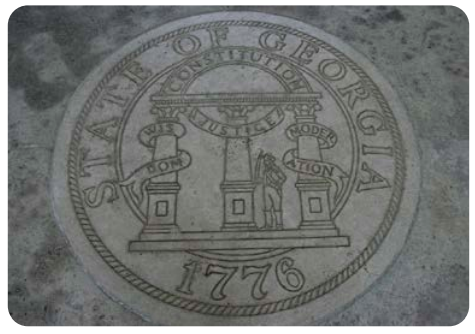 A picture of the Seal of the state of Georgia (dated 1776), engraved into stone. The description on the seal has three columns labeled “wisdom,” “justice,” and “moderation,” with a semi-circle labeled “constitution connecting the three.