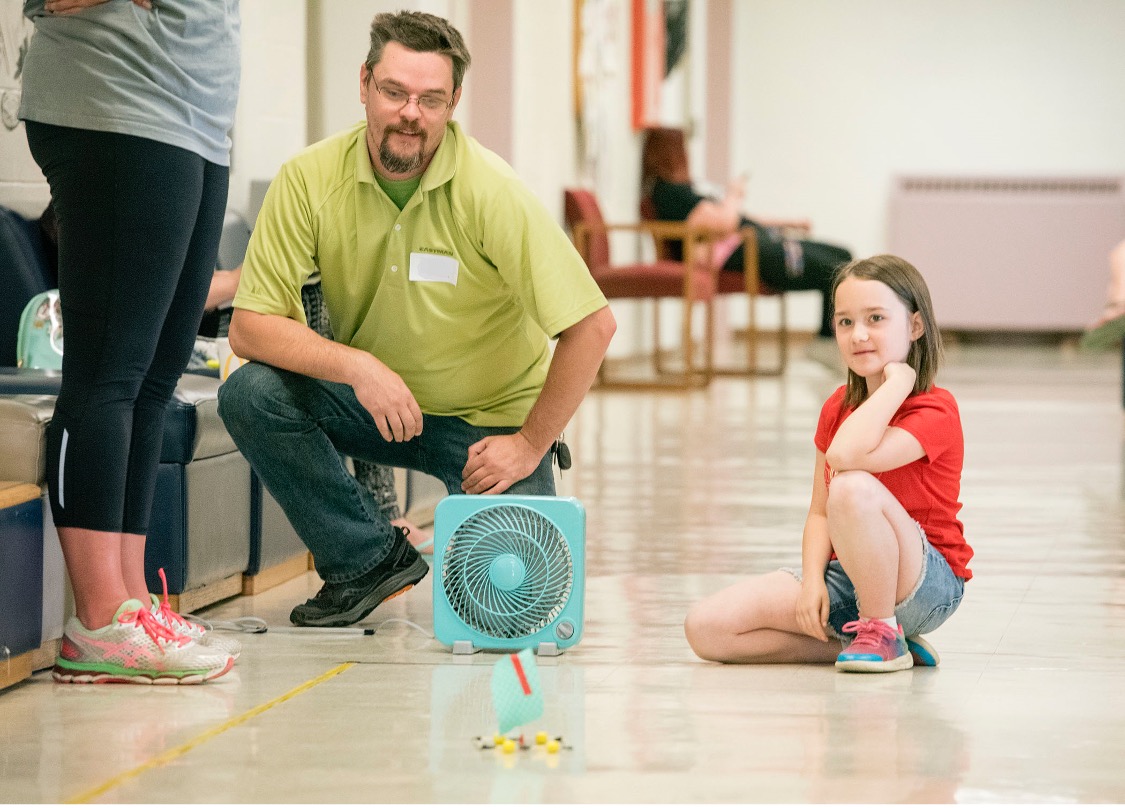 A student and a teacher watch as their sail project is tested in front of a fan.